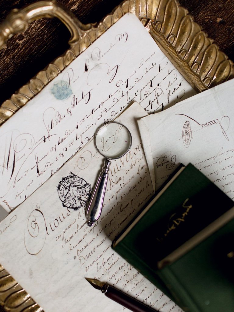 Top view of vintage papers with calligraphy, magnifying glass, and pen suggesting a vintage study.
